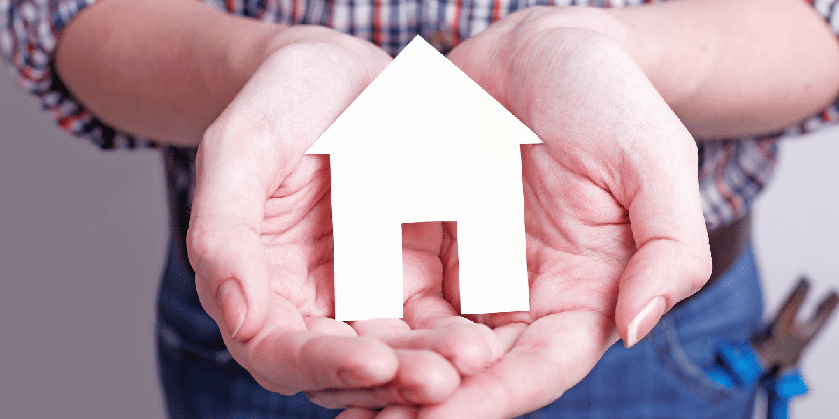 A person holding a small model house in a protective manner to demonstrate protecting the investment of a home